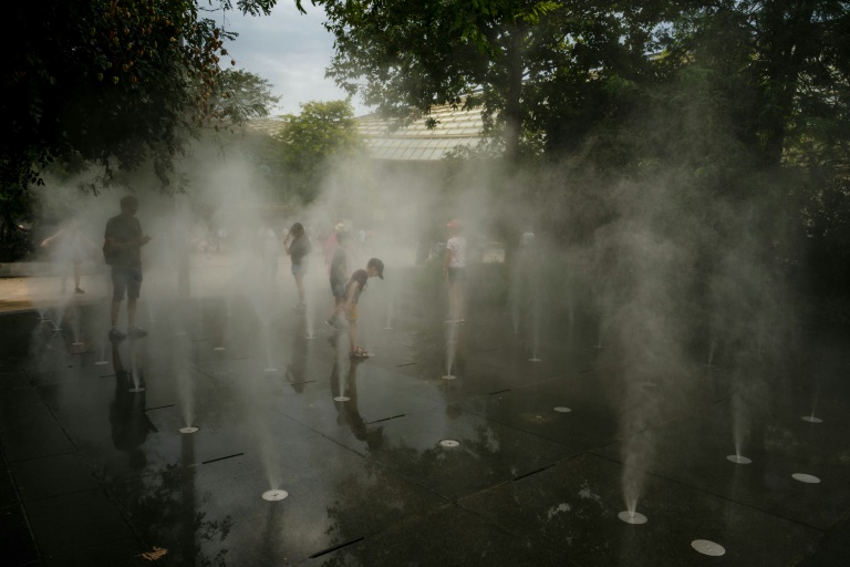 Des enfants se rafraîchissent dans une fontaine à brume dans le centre de Paris le 13 août 2025, en pleine canicule