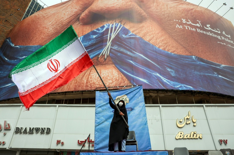 Une femme agite un drapeau iranien devant un panneau anti-américain sur la fermeture du détroit d'Ormuz, le 5 mai 2026 à Téhéran
