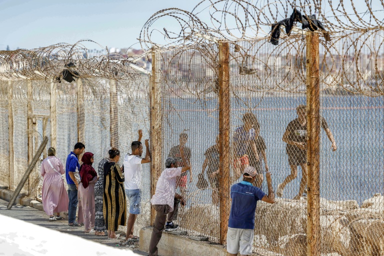 Des proches de migrants ayant traversé la frontière entre le Maroc et l'enclave espagnole de Ceuta voient passer des personnes refoulées derrière un grillage, dans la ville marocaine de Fnideq, le 2 août 2026