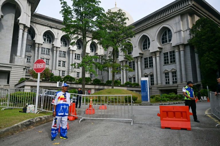 Un partisan de l'ex-Premier ministre malaisien Najib Razak (à gauche), habillé aux couleurs de son parti, se tient devant le palais de justice de Putrajaya, en Malaisie, le 26 décembre 2025