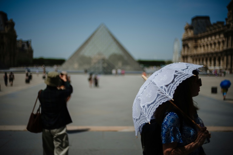 Une touriste se protège du soleil sous une ombrelle devant la Pyramide du Louvre, à Paris, le 23 juin 2026