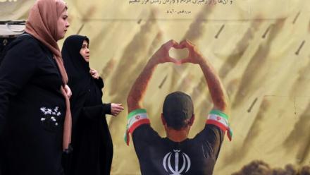 Des femmes passent devant une banderole représentant un homme faisant un cœur avec ses mains devant des tirs de missiles, à Téhéran le 19 avril 2026