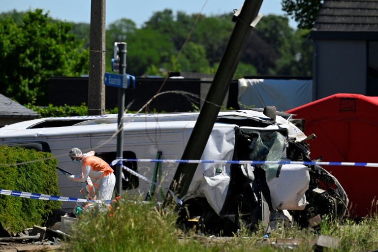 Un membre de la police scientifique inspecte les lieux à côté d'un bus endommagé après avoir été percuté par un train au passage à niveau de Vierhuizen à Buggenhout, au nord de Bruxelles, le 26 mai 2026 en Belgique