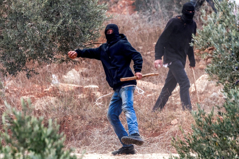 Un homme masqué lance des pierres sur des Palestiniens rassemblés pour la saison annuelle de la récolte des olives, lors d'une attaque de colons israéliens sur le village palestinien de Beita, au sud de Naplouse, en Cisjordanie occupée, le 10 octobre 2025