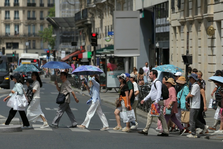 Des touristes se protègent du soleil sous des parapluies à Paris le 23 juin 2026
