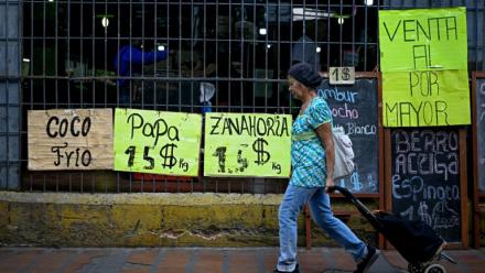 Une femme tire un chariot de courses à roulettes devant un supermarché qui affiche sur des panneaux les prix des aliments en dollars américains à Caracas, le 22 avril 2026