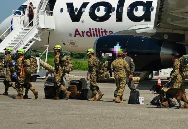 Des militaires salvadoriens accompagnés de chiens renifleurs se préparent à embarquer à bord d’un avion à destination du Venezuela, sur la base aérienne de Comalapa à San Luis Talpa, au Salvador, le 25 juin 2026