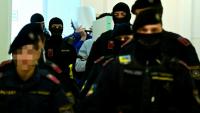 Deux accusés, escortés par des policiers, cachent leurs visages à leur arrivée à la salle d'audience du tribunal de Wiener Neustadt, en Autriche, le 28 avril 2026, pour un projet d'attentat lors d'un concert de Taylor Swift à Vienne