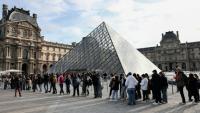 Des visiteurs font la queue devant la Pyramide du Louvre, conçue par l'architecte sino-américain Ieoh Ming Pei, et le musée du Louvre le jour de sa réouverture après un vol de bijoux, le 22 octobre 2025 à Paris
